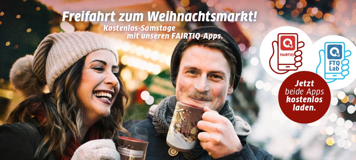 Eine Frau und ein Mann mit Schnäuzer trinken ein Heißgetränk aus einer Finni-und-Rudi-Adventstasse auf dem Weihnachtsmarkt. Der Mann schaut direkt zum Betrachter und lächelt. Die Frau steht links daneben und lacht herzlich. Auf dem Motiv steht in weißen Buchstaben: 