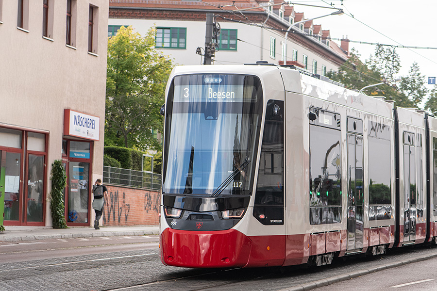 Moderne Straßenbahn der Linie 3 mit der Zielanzeige Beesen fährt auf städtischer Straße neben Wohngebäuden.