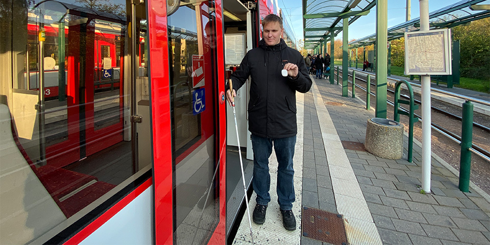 Blinder Fahrgast hält BIOS Sender in der Hand.