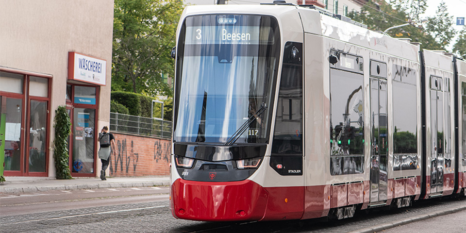 Moderne Straßenbahn der Linie 3 mit der Zielanzeige Beesen fährt auf städtischer Straße neben Wohngebäuden.