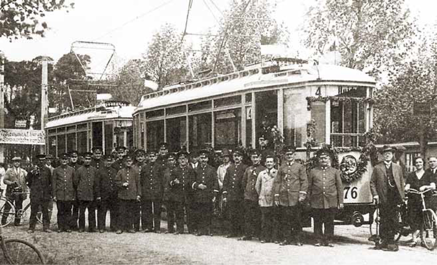 Eine schwarz-weiß-Aufnahme: Mehr als 10 Männer stehen in Uniform vor einer alten Straßenbahn.