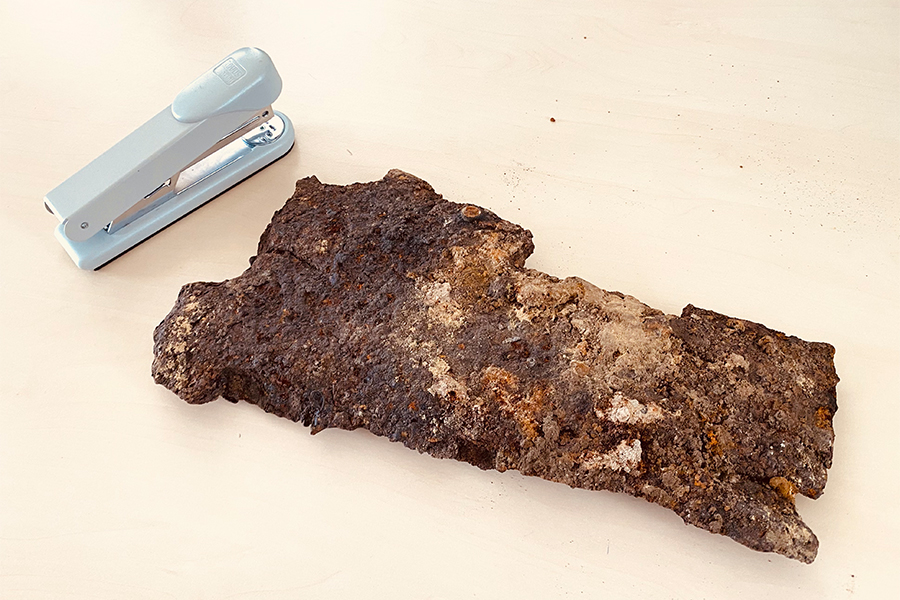 Ein Bombensplitter liegt neben einem Bürotacker auf einem Tisch.