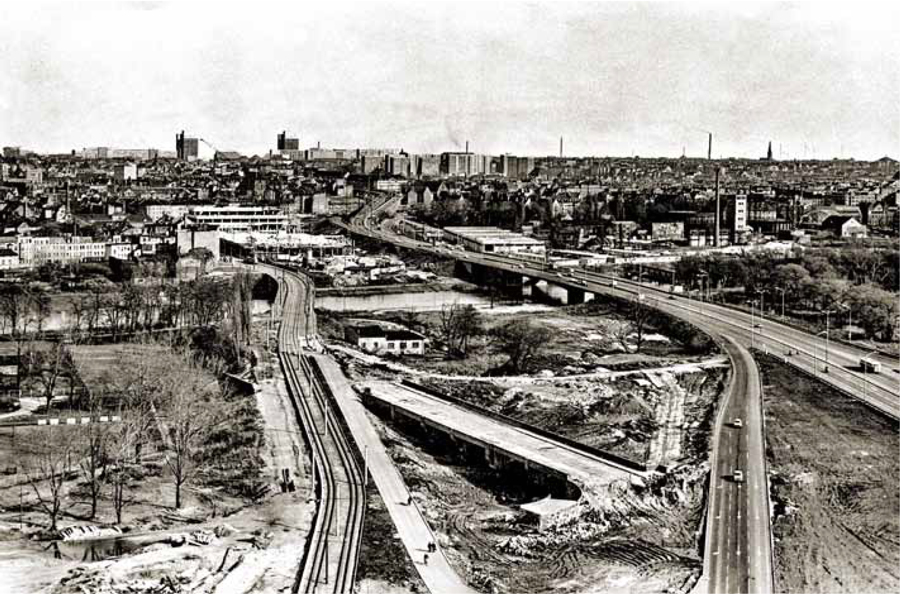Eine schwarz-weiß-Aufnahme von oben. Im Hintergrund ist das Stadtbild zu sehen. Im Vordergrund sind links und rechts die beiden Brücken.