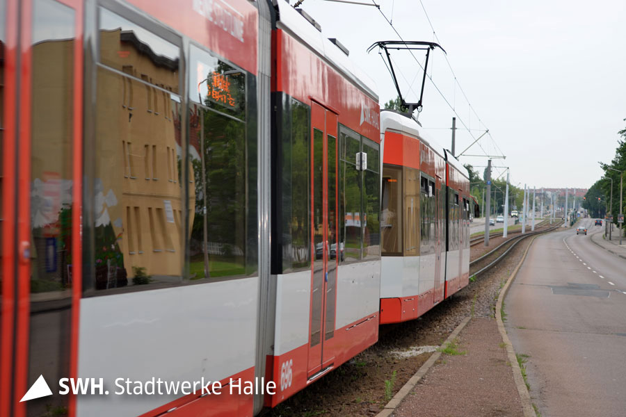 Eine rote Straßenbahn der HAVAG im Böllberger Weg. Die Bahn ist am linken Bildrand. Am rechten Bildrand sieht man die alte Straße. Der Himmel ist bedeckt.