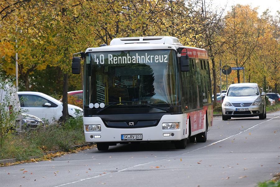 Ein weißer Bus mit der Aufschrift "40 Rennbahnkreuz" fährt auf einer Straße. Er ist von vorn fotografiert. Hinter dem Bus fährt noch ein silbernes Fahrzeug.