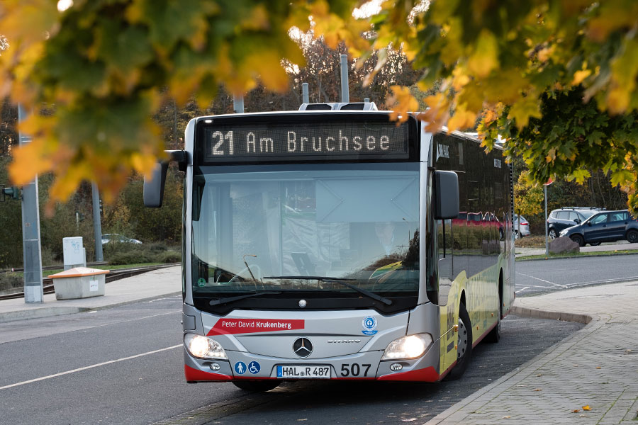 Ein silberner Bus der HAVAG bei der Einfahrt in eine Haltestelle. Am oberen Bildrand sind Blätter eines Baumes.
