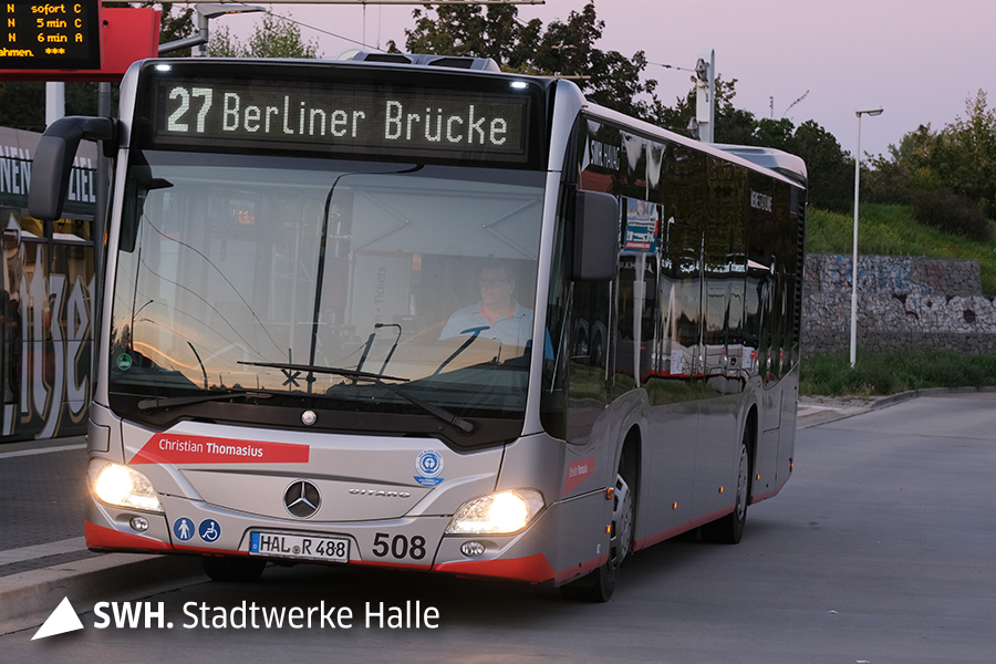 Ein silberner Bus der Marke Mercedes der Linie steht an einer Haltestelle. Die Zielaufschrift heißt "27 Berliner Brücke".