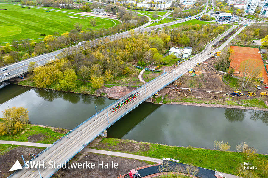 Eine Luftaufnahme der Elisabethbrücke in Richtung Halle-Neustadt. Die Brücke überquert die Saale. Auf der Brücke fährt eine Straßenbahn. 