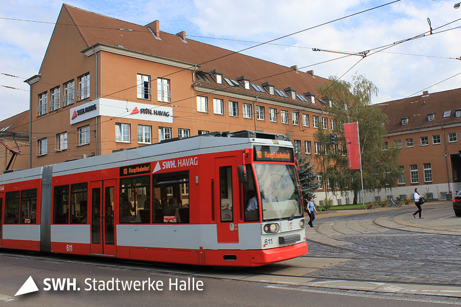 Eine rote Straßenbahn fährt von links nach rechts vor einem orangenen Backsteinhaus. 