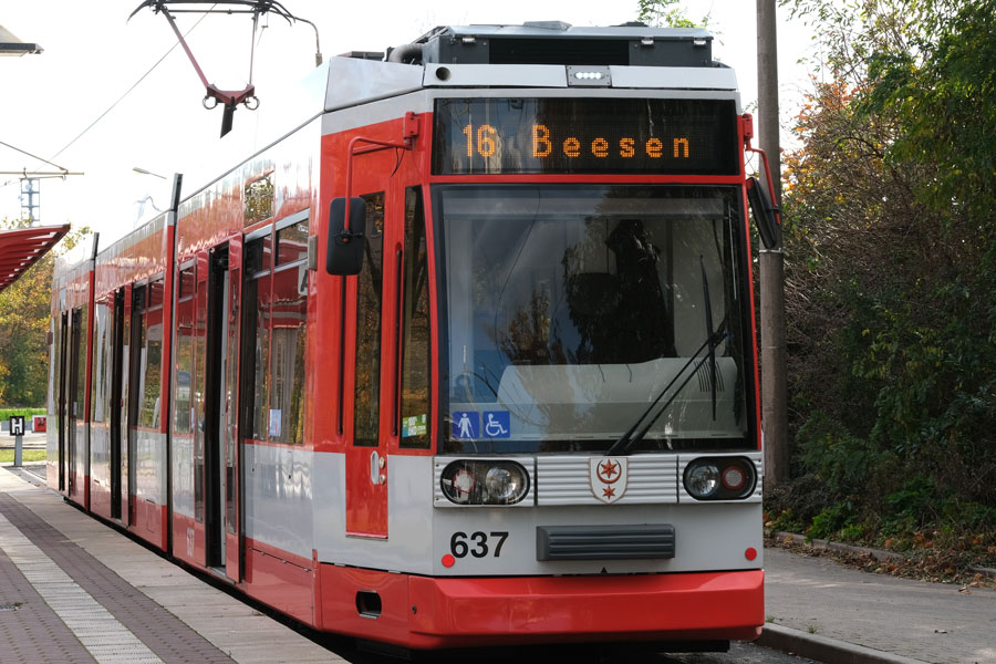 Eine Frontalaufnahme einer roten Straßenbahn mit der Zielbeschriftung "16 Beesen". Die Straßenbahn steht an der Haltestelle, die Türen sind geöffnet.