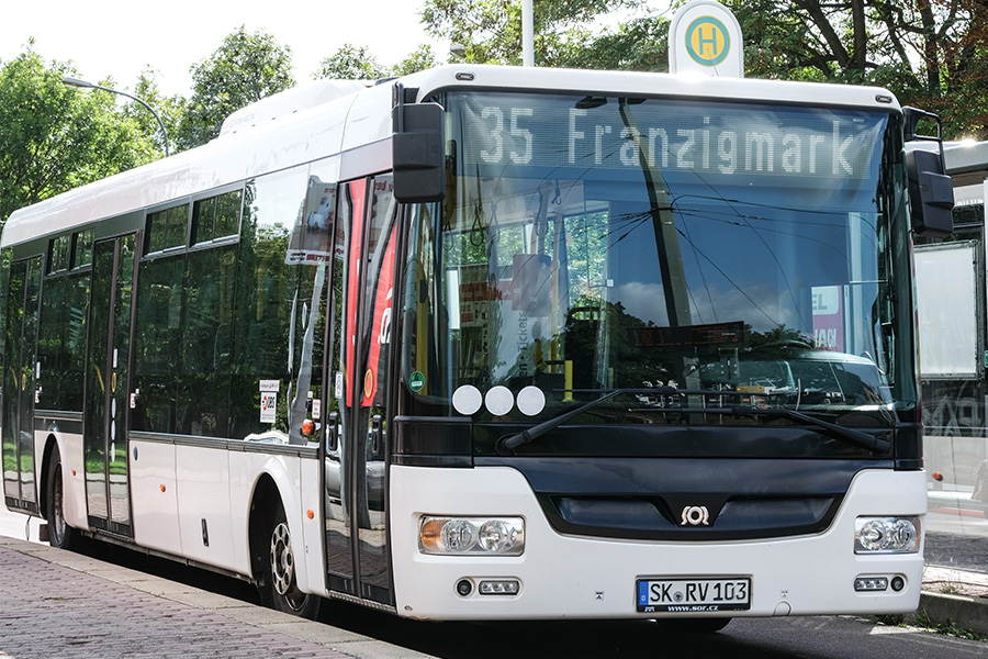 Ein weißer Bus wird gezeigt. In seiner Zielanzeige steht "35 Franzigmark". Der Bus steht an einer Haltestelle. Es sitzt keine Person im Bus.