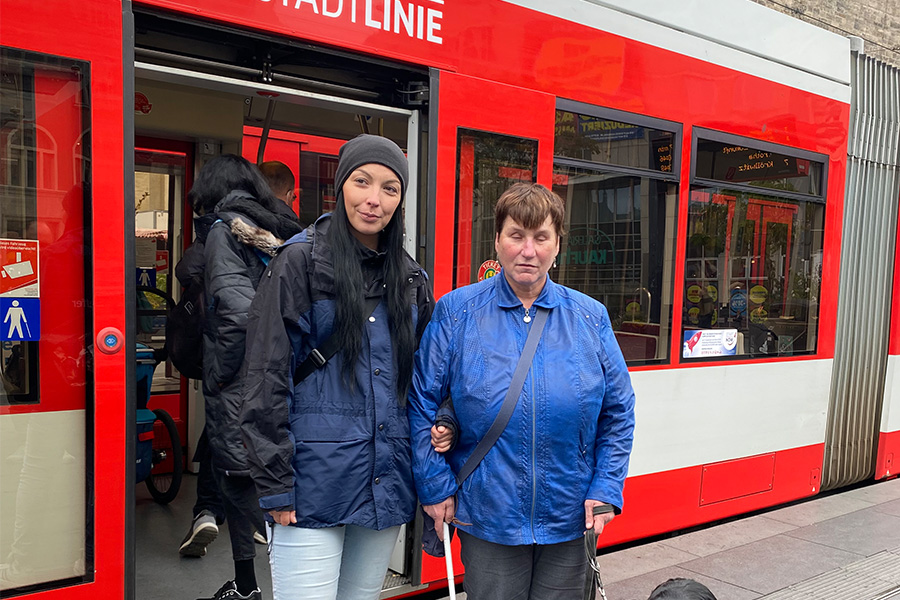 Eine Frau mit Blindenhund steht zusammen mit einer Mobilitätshelferin der SWH vor einer roten Straßenbahn an der Haltestelle Steintor.