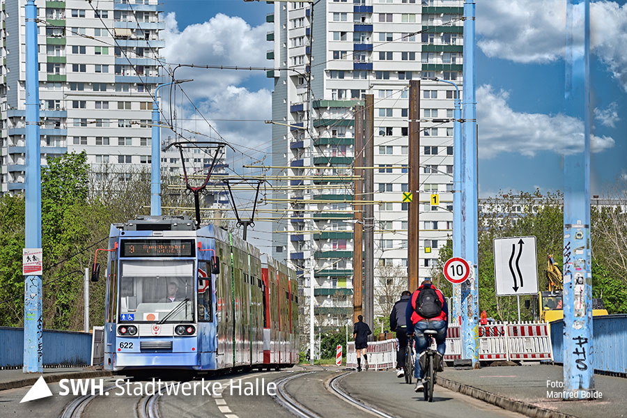 Ein Foto auf der mansfelder Straße. Auf der linken Seite kommt eine Straßenbahn gefahren. Recht radelt ein Fahrradfahrer. Im Hintergrund sind 2 Hochhäuser zu sehen.