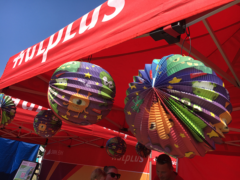 Zwei Laternen Lampions hängen vor einen Info-Stand der Stadtwerke Halle auf dem Laternenfest. Die Lampions haben kleine illustierte Monster aufgedruckt.