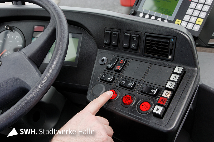 Detailaufnahme eines Fingers, der einen Knopf auf einer Bedienoberfläche in einer Fahrer*innenkabines eines Busses betätigt.