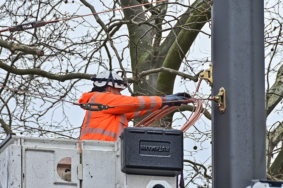 Mitarbeiter bringt Querfeldbefestigung an Mast an.