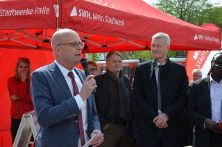 Dr. Bernd Wiegand, Oberbürgermeister der Stadt Halle (Saale), hat ein Mikro in der Hand und spricht zu den Gästen. Im Hintergrund ist ein rotes Stadtwerke-Zelt.
