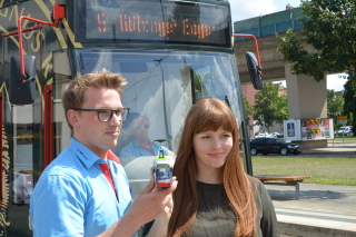 Florian Henze und Therese Kästner freuen sich über den Preis für ihre Forschungsarbeit. Im Hintergrund ist eine Straßenbahn.