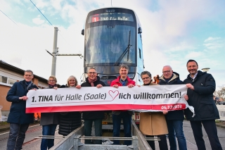 Die Gäste stehen vor der neuen TINA und halten ein Transparent hoch auf dem steht: 1. TINA für Halle (Saale)