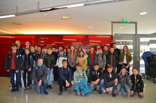 33 junge Schülerinnen und Schüler haben sich im Kundencenter der Stadtwerke Halle vor einer roten Wand für ein Gruppenfoto aufgestellt.