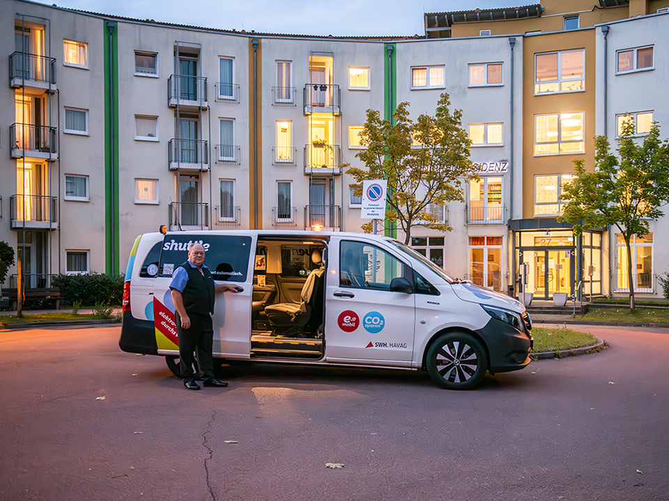 Ein Fahrer steht neben einem movemix_shuttle in der Abenddämmerung.