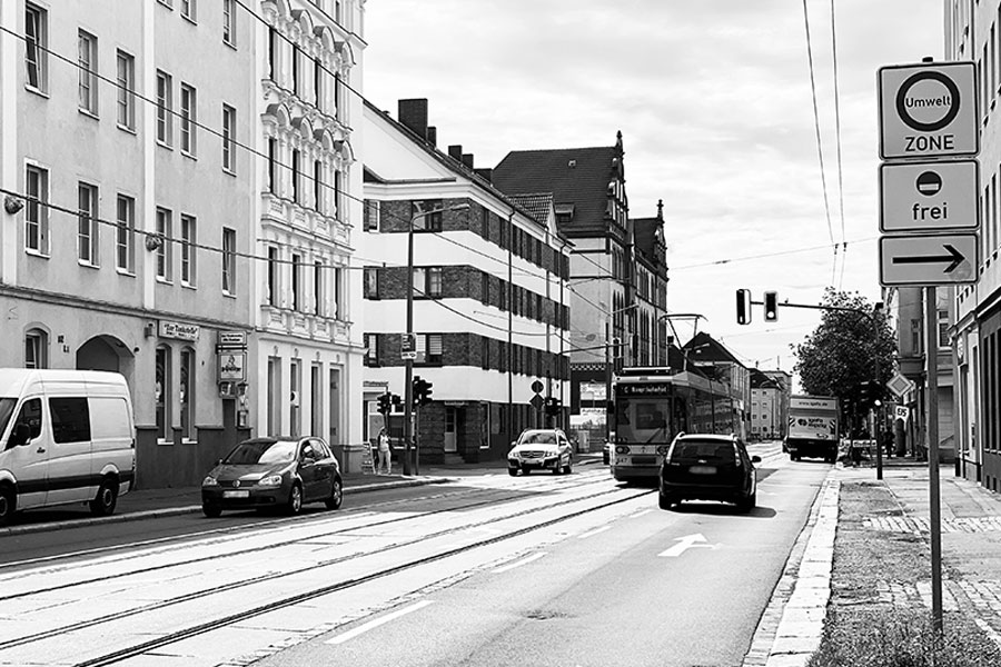 Ein Schwarz-Weiß-Bild: Eine Straßenbahn fährt zwischen Autos auf einer breiten Straße.