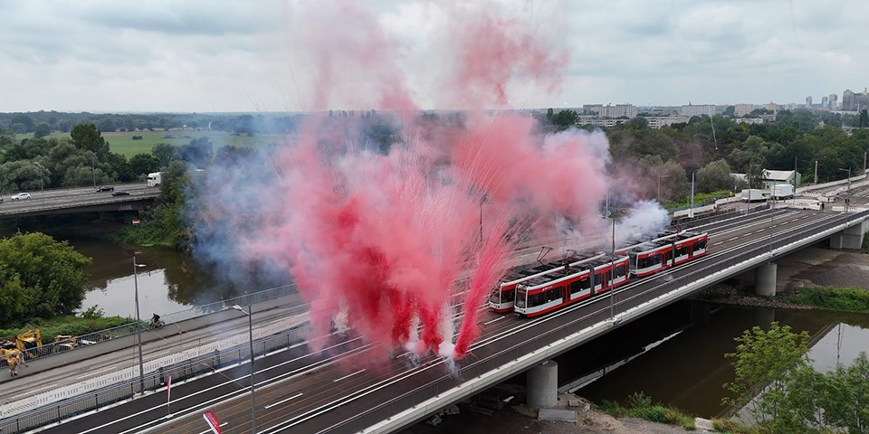 Straßenbahn fährt über neue Brücke, im Vordergrund kleines Feuerwerk.