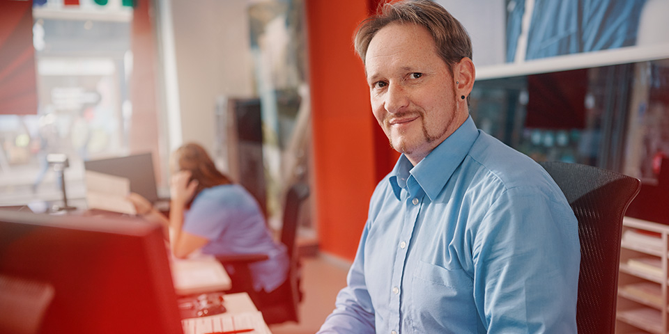 Ein Mitarbeiter aus unserem Service-Center lächelt in die Kamera.