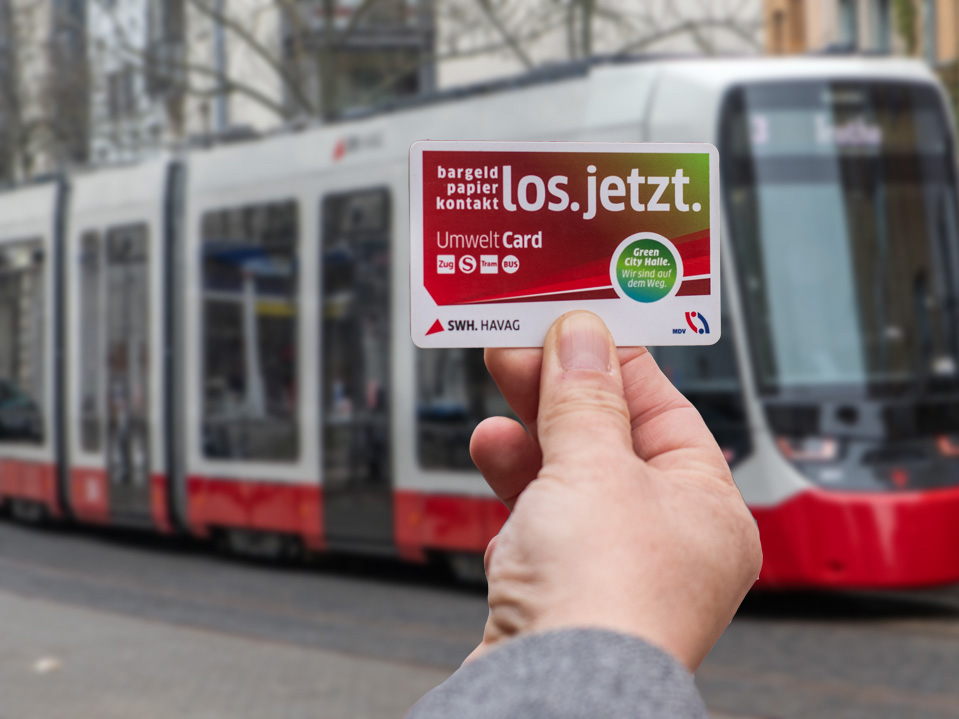 Eine Hand hält die Abo-Chipkarte, im Hintergrund ist eine TINA-Straßenbahn.