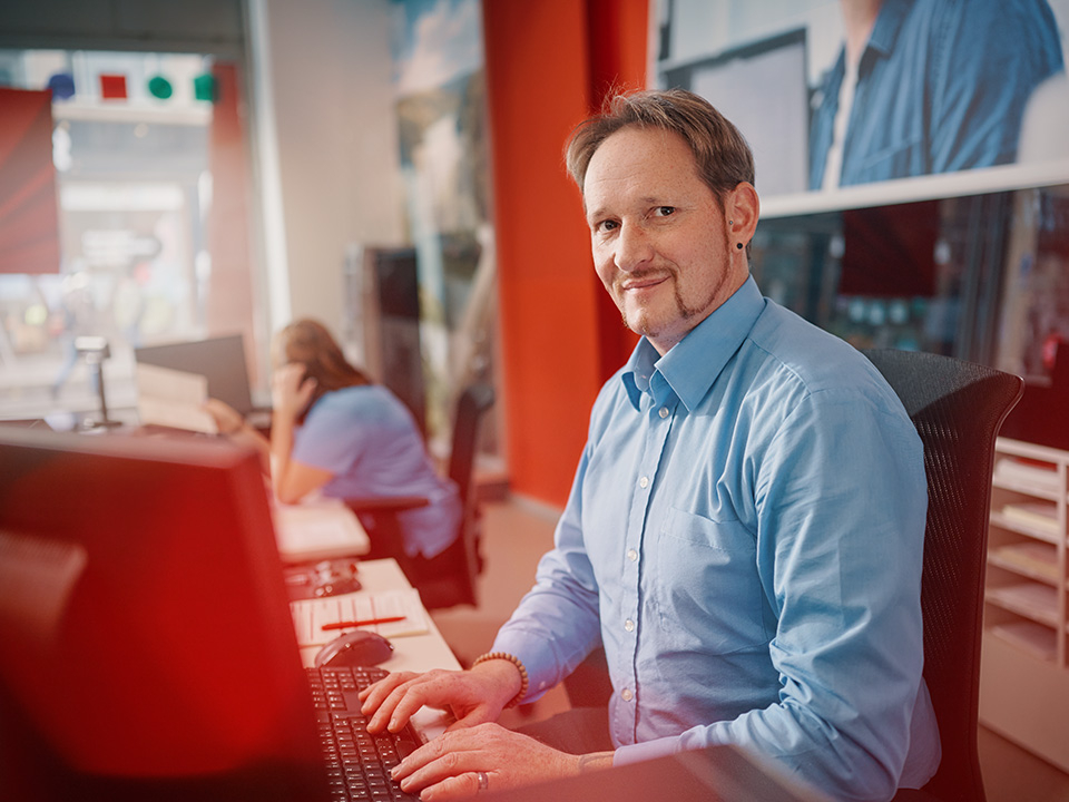 Ein Mitarbeiter aus unserem Service-Center lächelt in die Kamera.